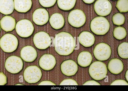 Une photo plate de petites tranches de courgettes disposées sur un tapis séchant au soleil Banque D'Images