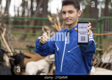 Vétérinaire montrant l'écran d'un téléphone portable avec la vaccination d'un animal dans une ferme caprine Banque D'Images