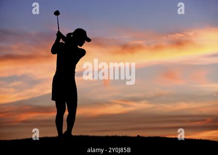 Une silhouette d'une femme golfeuse au coucher du soleil balançant le club de golf Banque D'Images