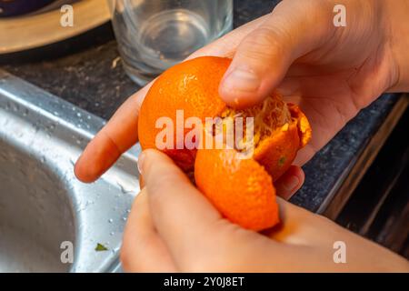 Gros plan des mains d'un enfant épluchant une orange mandarine. Banque D'Images