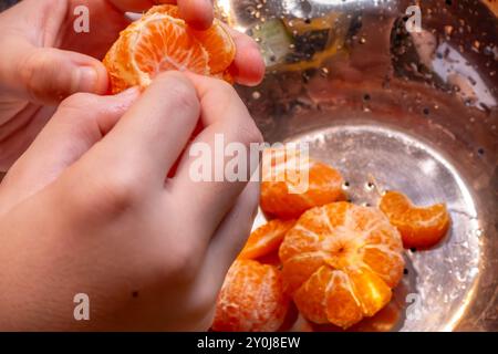 Gros plan des mains d'un enfant qui divisent des mandarines pelées en segments. Banque D'Images