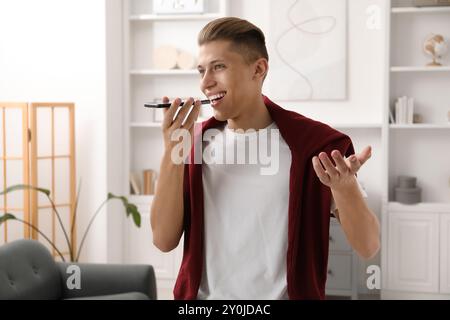 Jeune homme enregistrant un message vocal via smartphone à la maison Banque D'Images