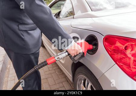 Personne pompant du gaz. Essence essence pour voiture à la buse de station d'essence dans le réservoir. Gros plan du pistolet de ravitaillement manuel et rouge. Banque D'Images