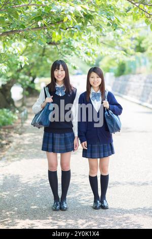 Deux lycéennes japonaises debout sur une route bordée d'arbres Banque D'Images