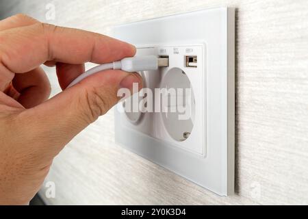 Débranchement du câble USB de l'adaptateur secteur. Débranchez le cordon USB du chargeur de téléphone portable. Homme tenant la fiche USB contre le chargeur mural. Connecteur enfichable int Banque D'Images