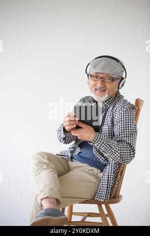 Homme senior portant une tablette tout en écoutant quelque chose sur un casque Banque D'Images