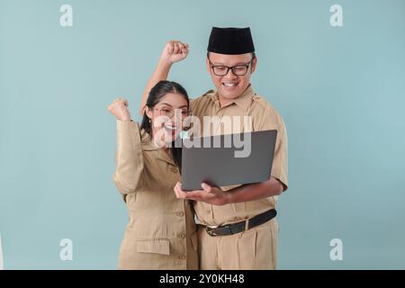 Deux employés du gouvernement indonésien excités portant un uniforme kaki tenant un ordinateur portable avec une expression heureuse et réussie. PNS et concept de fonctionnaire. Banque D'Images