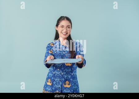 Femme joyeuse employée du gouvernement indonésien portant un uniforme de batik bleu et des lunettes présentant un rapport de document. PNS concept de fonctionnaire. Banque D'Images
