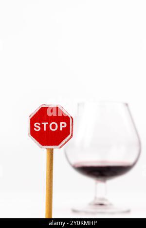 Une photo verticale avec un panneau stop en bois dans les détails nets, avec un verre à vin positionné derrière elle. L'arrière-plan blanc améliore la mise au point sur les s. Banque D'Images