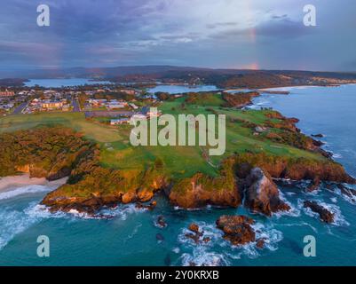 Vue aérienne d'un éclairage spectaculaire et d'un arc-en-ciel faible au-dessus d'un promontoire vert et d'une côte accidentée à Narooma sur la côte sud de la Nouvelle-Galles du Sud Banque D'Images