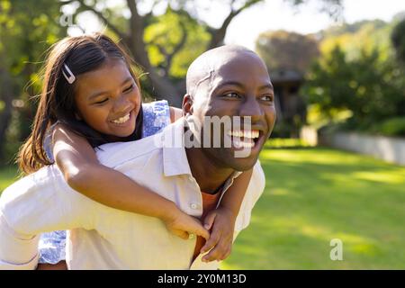 Père donnant à sa fille un tour de piggyback, à la fois souriant et profitant du temps en plein air Banque D'Images