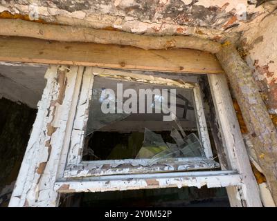 Gros plan d'une fenêtre brisée dans un vieux bâtiment abandonné. La peinture écaillée et le bois délabré suggèrent la négligence et la pourriture au fil du temps. Banque D'Images