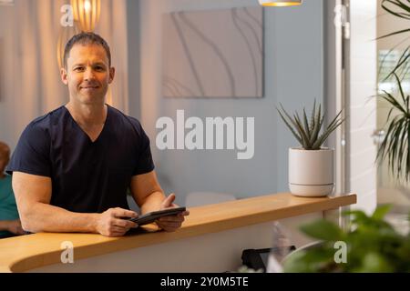 Tenant la tablette, médecin masculin, travailleur de la santé dans les gommages souriant à la réception dans la clinique, espace de copie Banque D'Images
