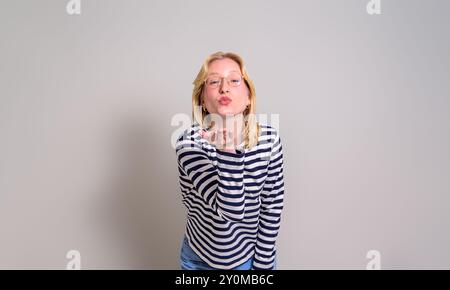 Portrait d'amour belle femme soufflant un baiser à la caméra tout en se tenant debout sur fond blanc Banque D'Images