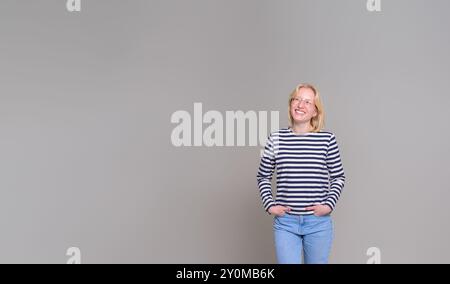 Jeune femme d'affaires souriante avec les mains dans les poches regardant loin et contemplant sur fond blanc Banque D'Images