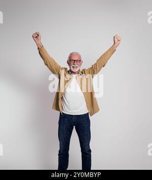 Professionnel masculin senior excité avec les bras levés souriant à la caméra et debout sur fond blanc Banque D'Images