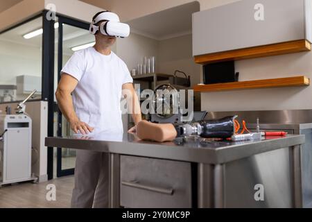 En utilisant un casque VR, homme travaillant dans un laboratoire prothétique avec un membre artificiel sur la table, copiez l'espace Banque D'Images