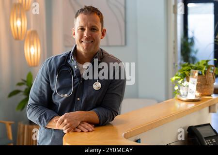 Médecin souriant avec stéthoscope appuyé sur le bureau de réception dans le cabinet médical Banque D'Images