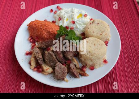 Une assiette de kebab d'agneau avec muhammara, couscous, lebneh et grenade. Banque D'Images