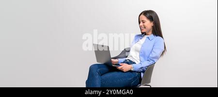 Professionnel féminin souriant faisant des recherches en ligne sur ordinateur portable sur chaise sur fond blanc Banque D'Images