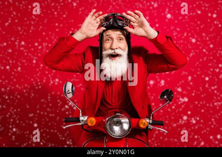 Photo de l'âge assez impressionné gentleman porter le nouveau costume de l'année coiffeur équitation bras moto lunettes isolé rouge couleur fond Banque D'Images
