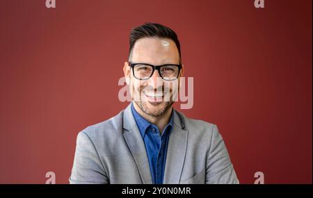 Portrait en gros plan d'un jeune homme d'affaires souriant dans des lunettes posant sur fond rouge isolé Banque D'Images