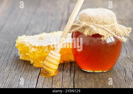 Morceau de nid d'abeille, miel liquide frais organique dans un pot en verre avec un plongeur sur fond en bois, nourriture saine Banque D'Images