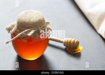 Miel liquide frais biologique dans un pot en verre ou un bol avec un plongeur sur fond rustique, nourriture saine Banque D'Images
