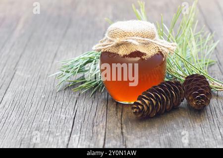 Miel de pin dans un pot ou un bol avec bâton de miel et pommes de pin sur une table rustique en bois, nourriture saine Banque D'Images