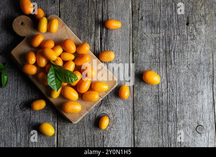 Fruits kumquat frais mûrs avec planche à découper ou sac en toile de jute sur fond en bois, margarita fortunella Banque D'Images