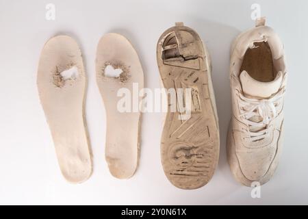 Ancienne sneaker blanche usée avec semelle partiellement détachée et semelle intérieure manquante. Saleté, usure et trous visibles dans la chaussure. La semelle et la semelle intérieure retirées sont lly Banque D'Images