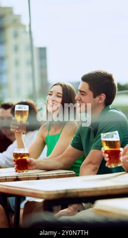 Jeune homme barbu aime la bière froide dans un cadre extérieur détendu, savourant moment. La femme est assise à proximité. Ambiance festive. Banque D'Images