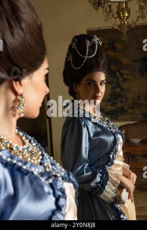 Belle jeune femme habillée dans le style rococo reine Marie Antoinette et portant une perruque authentique posant dans un intérieur de château français Banque D'Images