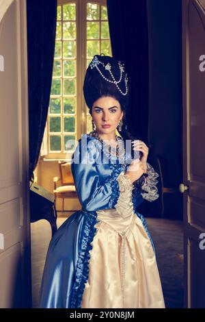 Belle jeune femme habillée dans le style rococo reine Marie Antoinette et portant une perruque authentique posant dans un intérieur de château français Banque D'Images