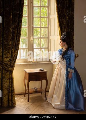 Belle jeune femme habillée dans le style rococo reine Marie Antoinette et portant une perruque authentique posant dans un intérieur de château français Banque D'Images