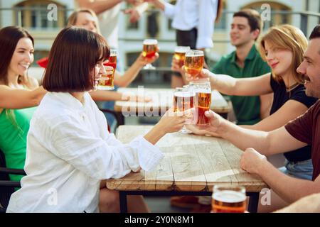 Les amis se rassemblent autour de la table, levant leurs verres en pain grillé aux bons moments. Ambiance animée et rire partagé pour une journée ensoleillée parfaite. Banque D'Images