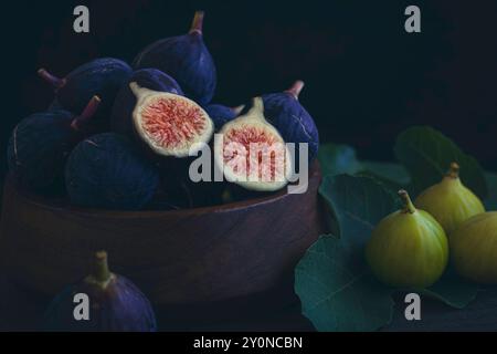 Figues violettes et vertes fraîchement cueillies un bol en bois avec des feuilles de figues Banque D'Images