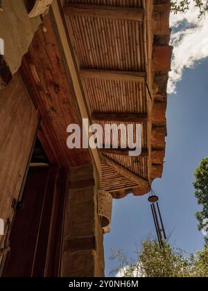 Vue partielle sur le toit et l'entrée d'une maison de campagne, avec un carillon métallique à l'arrière-plan, dans une ferme près de la ville de Villa de Leyva. Banque D'Images