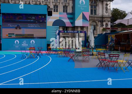 Paris 2024. Tôt le matin dans la zone des fans des Jeux Paralympiques. Chaises de jardin françaises vides colorées sur la piste de course avec un grand écran. Banque D'Images