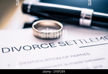 Un document d'entente de règlement de divorce avec une bague de mariage et un stylo placés sur le dessus, symbolisant la fin d'un mariage et les processus juridiques impliqués Banque D'Images