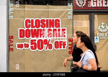 Jeune femme (avec flou de mouvement) marchant près d'un signe de vente de fermeture sur une vitrine de Princes Street, Édimbourg, Écosse, Royaume-Uni. Banque D'Images