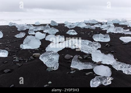 Diamond Beach en Islande - bergs de glace transparents lavés à terre sur la plage de sable noir avec paysage marin en arrière-plan. Banque D'Images