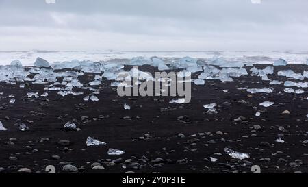 Diamond Beach en Islande - bergs de glace transparents lavés à terre sur la plage de sable noir avec paysage marin en arrière-plan. Banque D'Images