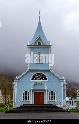 L'église bleue de Seydisfjordur (Seydisfjardarkirkja), vue extérieure de la façade du bâtiment bleu vif, montagnes brumeuses en arrière-plan, Islande. Banque D'Images