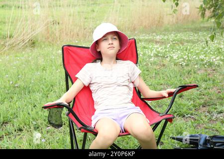 Fille mignonne se reposant dans une chaise de camping à l'extérieur Banque D'Images