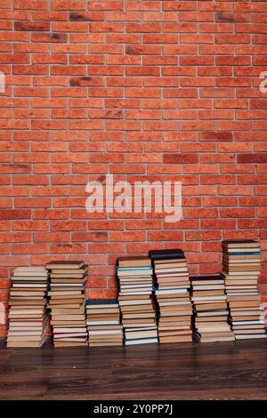 beaucoup de piles de livres éducatifs par le mur de briques dans la bibliothèque comme arrière-plan Banque D'Images