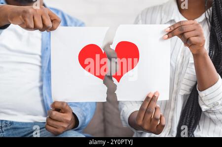 Black couple déchirant le papier avec le symbole de coeur rouge en moitiés Banque D'Images