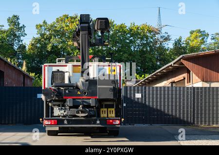 Une vue arrière d’un camion-grue garé à une entrée, positionné entre deux bâtiments et devant un portail noir, prêt à travailler. Banque D'Images