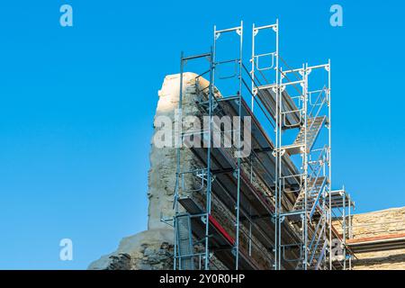 Une grande structure d'échafaudage soutient les efforts de restauration en cours sur d'anciennes ruines de pierre. Le ciel dégagé offre une toile de fond lumineuse pendant que les travailleurs se préparent Banque D'Images