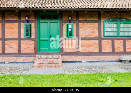 Un charmant bâtiment en brique avec une porte verte vibrante et des fenêtres, situé dans une zone rurale accueillante entourée de verdure Banque D'Images